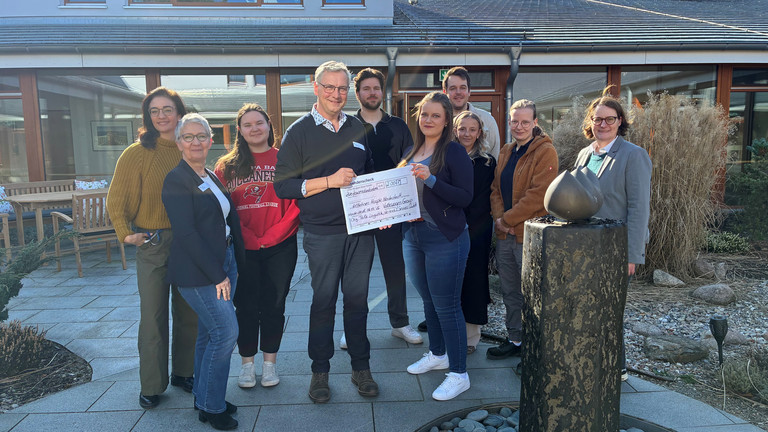Mitarbeitende der VW Group Norderstedt überreichen symbolisch einen Spendenscheck an Einrichtungsleiter Jens Klindworth und andere Mitarbeitende aus dem Albertinen Hospiz Norderstedt für die Hospizarbeit im Hospizgarten vor dem Hospiz.