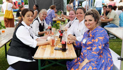 Mehrere Mitarbeitende sitzen an einer Bierbank mit Essen und Getränken und blicken in die Kamera beim Sommerfest 2026 auf dem Gesundheitscampus Volksdorf des Evangelischen Amalie Sieveking Krankenhauses, der Residenz am Wiesenkamp, des Feierabendhauses Volksdorf und der Albertinen Kindertagesstätte Volksdorf. Mehrere Mitarbeitende sitzen an einer Bierbank mit Essen und Getränken und blicken in die Kamera beim Sommerfest 2026 auf dem Gesundheitscampus Volksdorf des Evangelischen Amalie Sieveking Krankenhauses, der Residenz am Wiesenkamp, des Feierabendhauses Volksdorf und der Albertinen Kindertagesstätte Volksdorf.