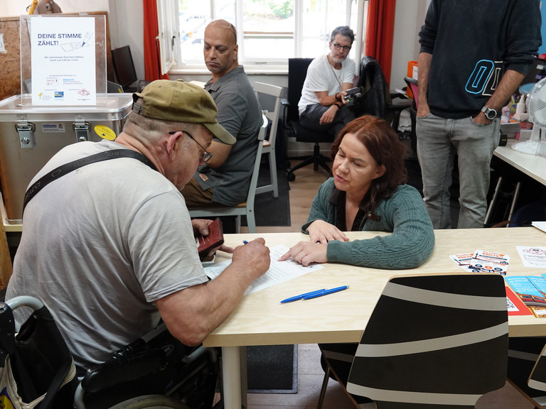 Frau hilft einem Mann beim Eintragen in das Wahlverzeichnis und beim Beantragen der Briefwahlunterlagen in der Tagesstätte des Sozialprojekts Prenzlauer Berg von Immanuel Beratung