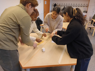 Vier Auszubildende arbeiten gemeinsam an einem Tisch an einem Turm aus Spaghetti und Marshmallows und stimmen ihre nächsten Bauschritte ab.